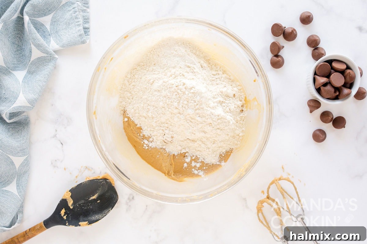 Adding flour mixture to the peanut butter cookie dough in a bowl, showing the mixing process.