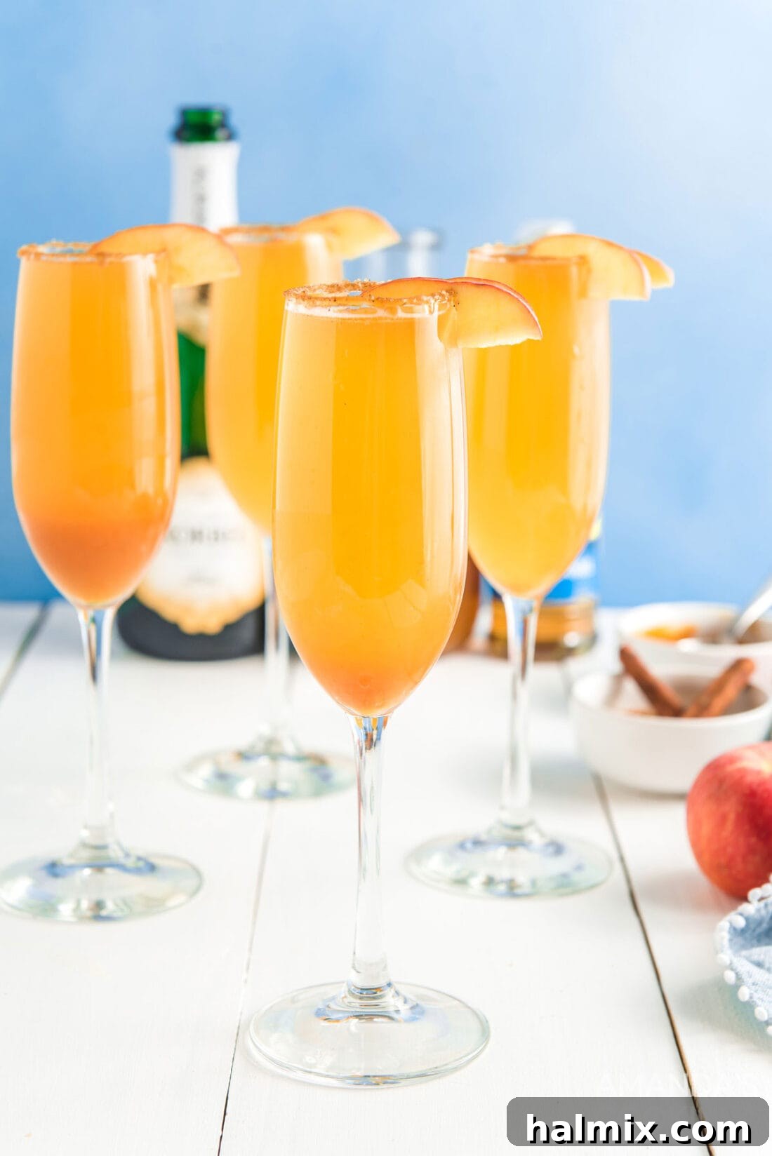 Four glasses of sparkling caramel apple mimosas garnished with apple slices and a cinnamon sugar rim.