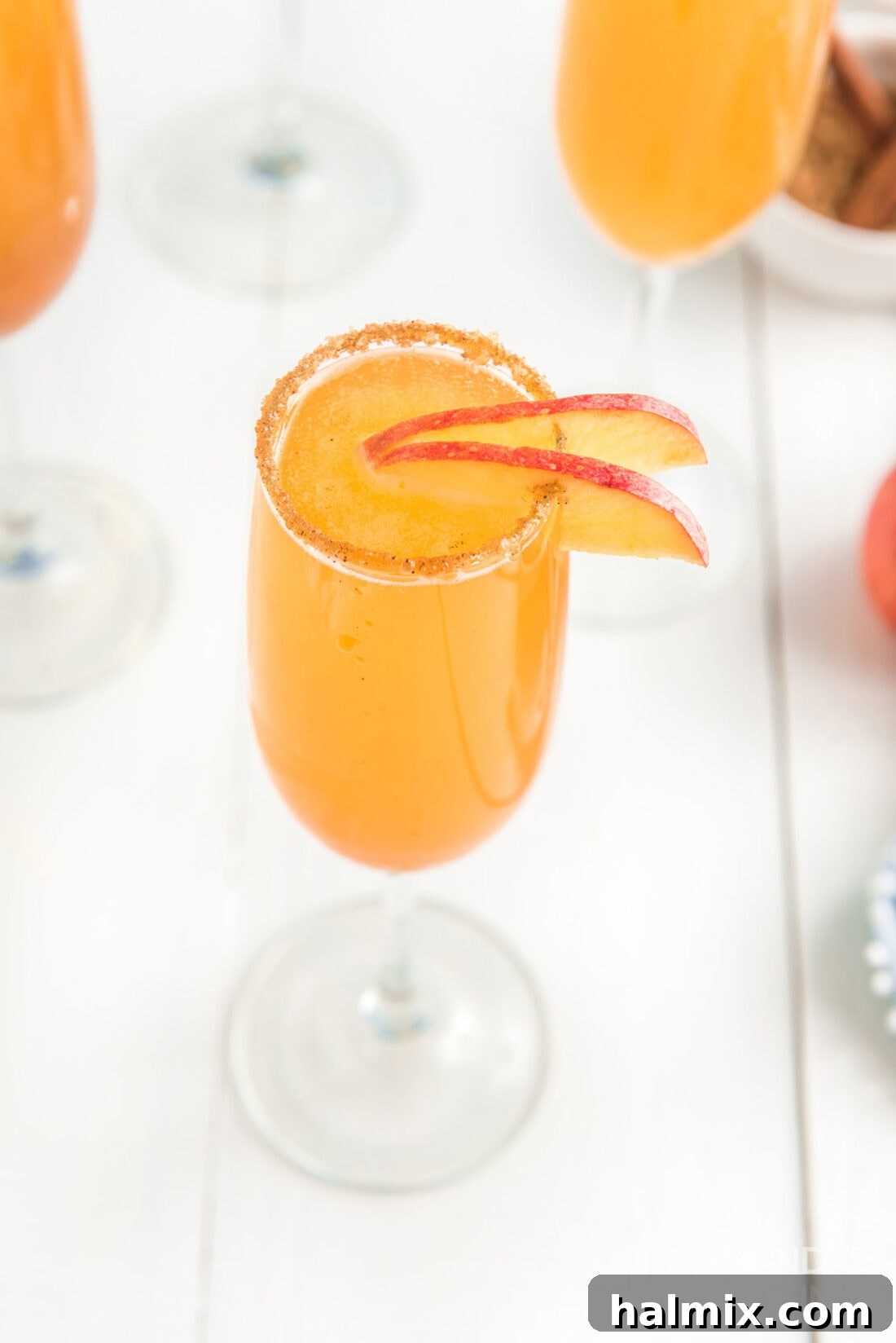 A single glass of caramel apple mimosa with a fresh apple slice and cinnamon sugar rim.