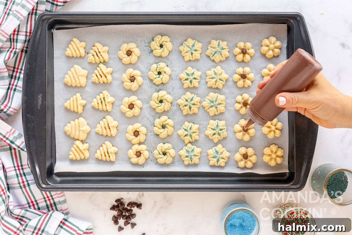 close-up of a hand adding chocolate drizzle to cooled spritz cookies