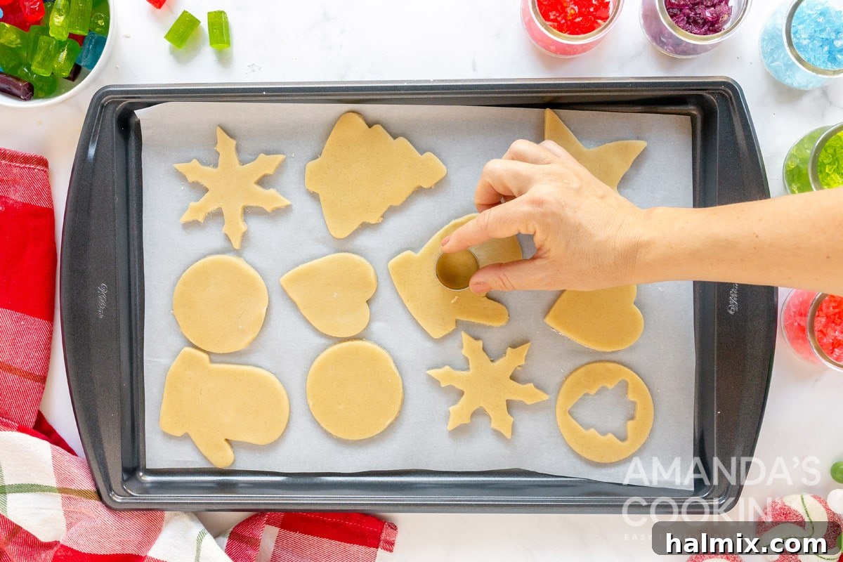 A smaller cookie cutter being used to cut out the center of a larger cookie dough shape on a baking sheet.