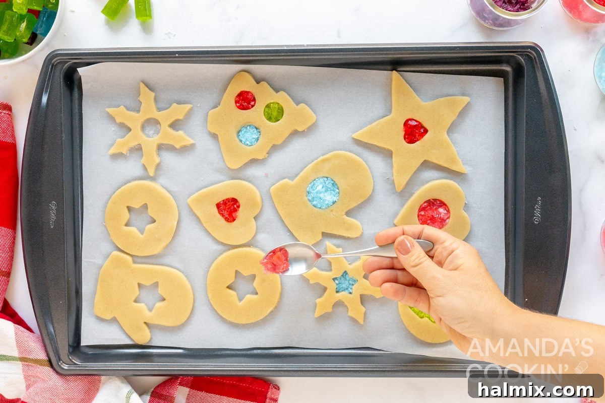Close-up of cookie dough cut-outs filled with vibrant crushed candies on a baking sheet, ready for baking.