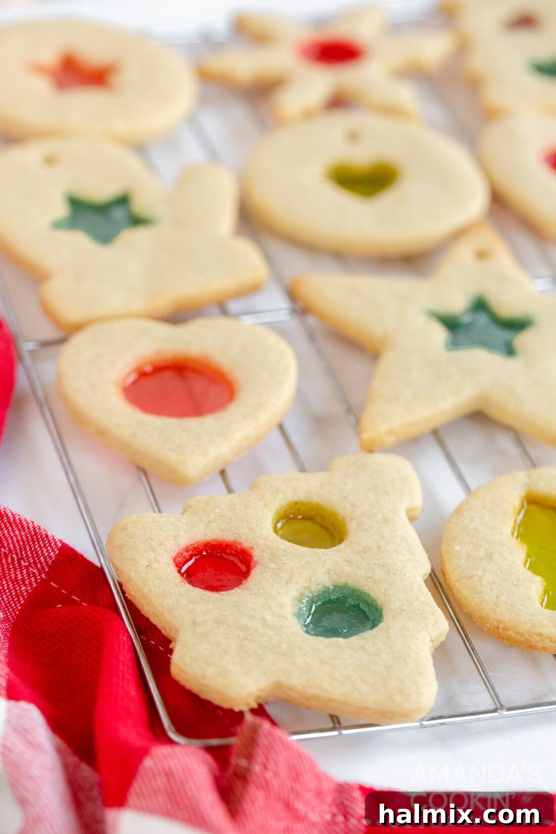 Assortment of festive stained glass cookies, including snowflakes, stars, and other holiday shapes, cooling on a wire rack.