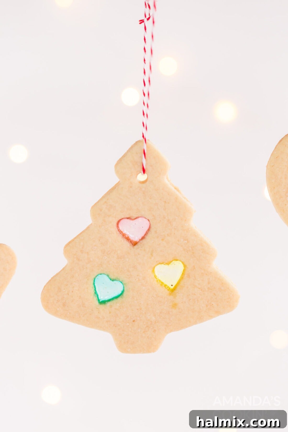 A festive stained glass cookie with a red ribbon tied through a small hole, ready to be hung as a Christmas tree ornament.