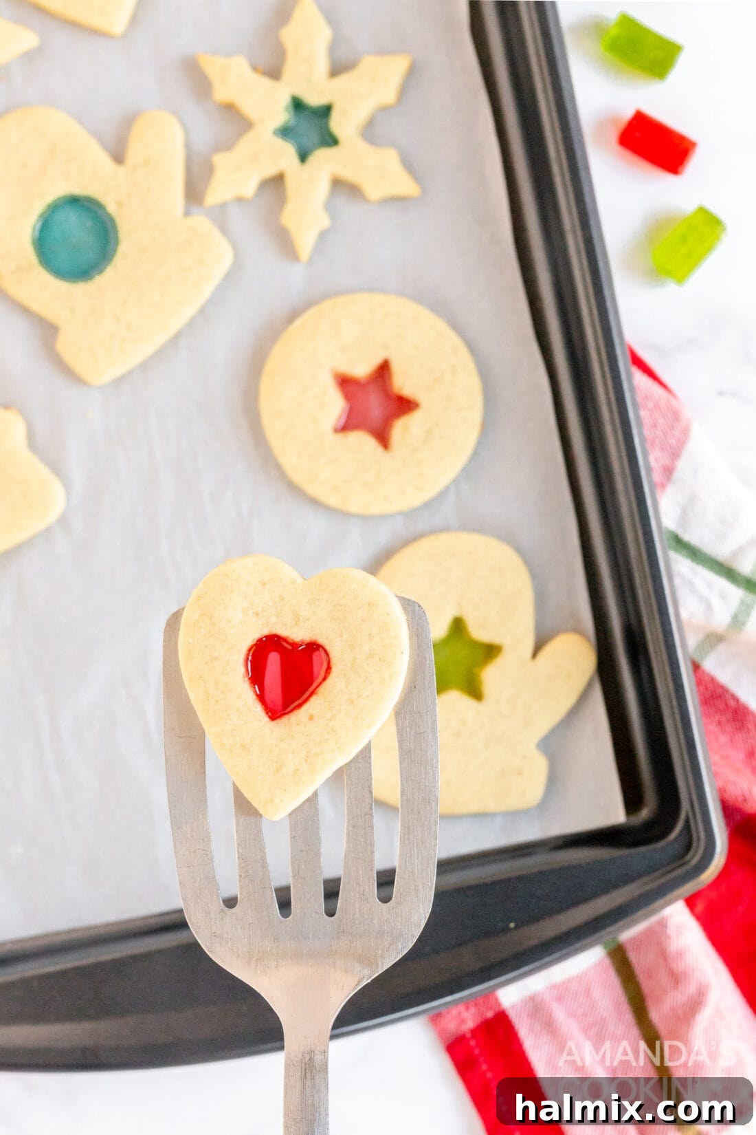 A spatula gently lifting a freshly baked stained glass cookie from a baking sheet, showcasing its perfect golden-brown edges and vibrant candy center.