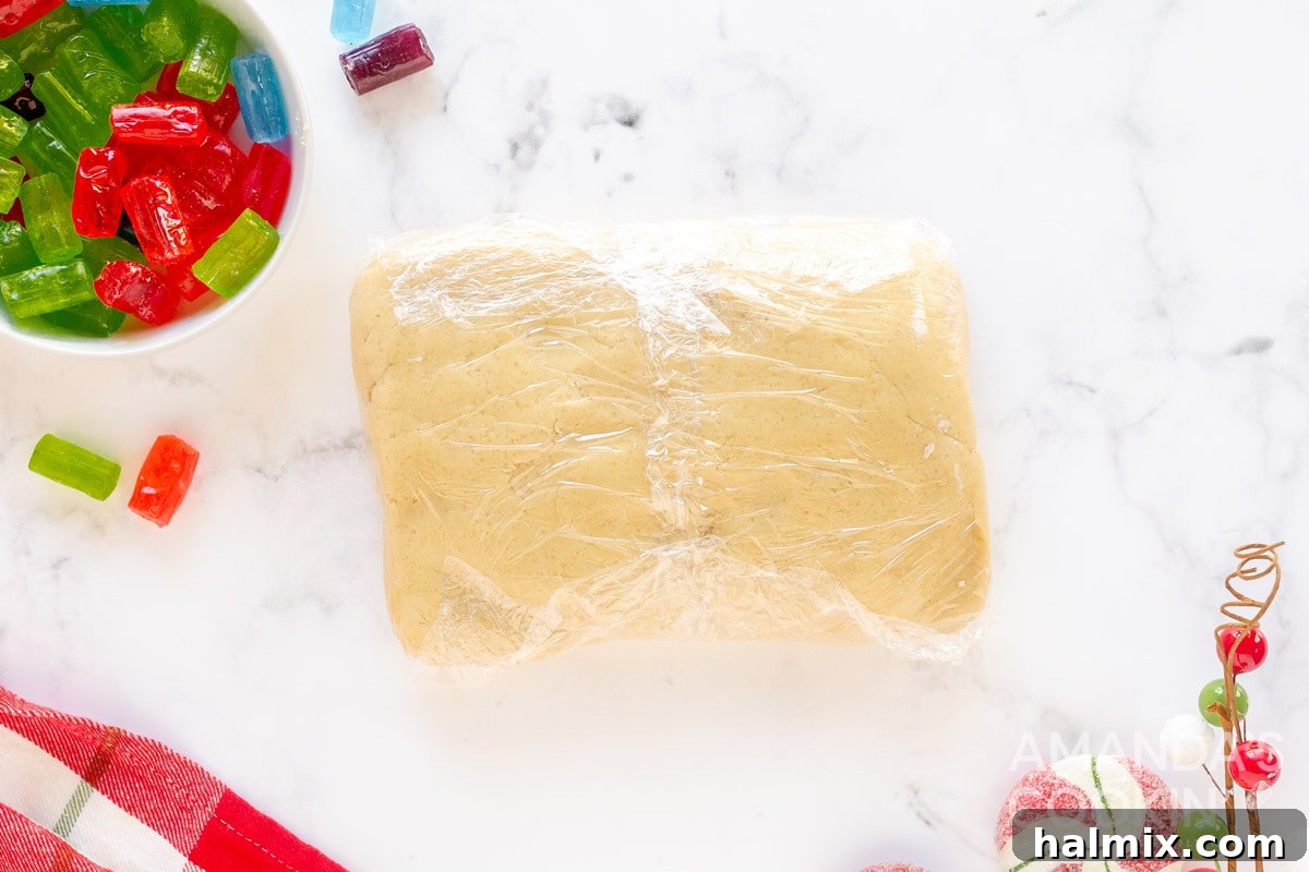 Round cookie dough disc wrapped securely in plastic wrap, chilling in the refrigerator.