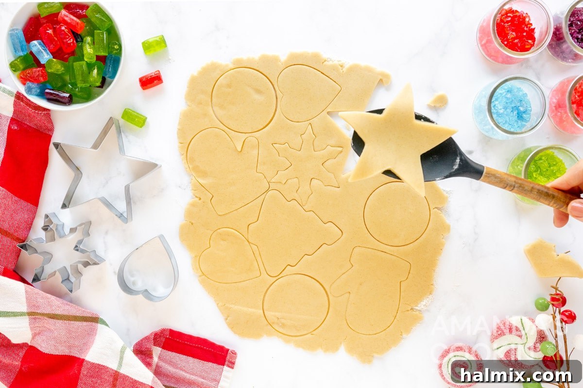 Cookie dough rolled out on a floured surface with several large shapes already cut out using cookie cutters.