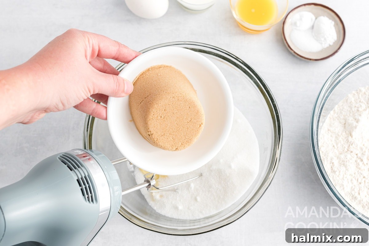 Adding brown sugar to creamed butter and granulated sugar in a mixing bowl.