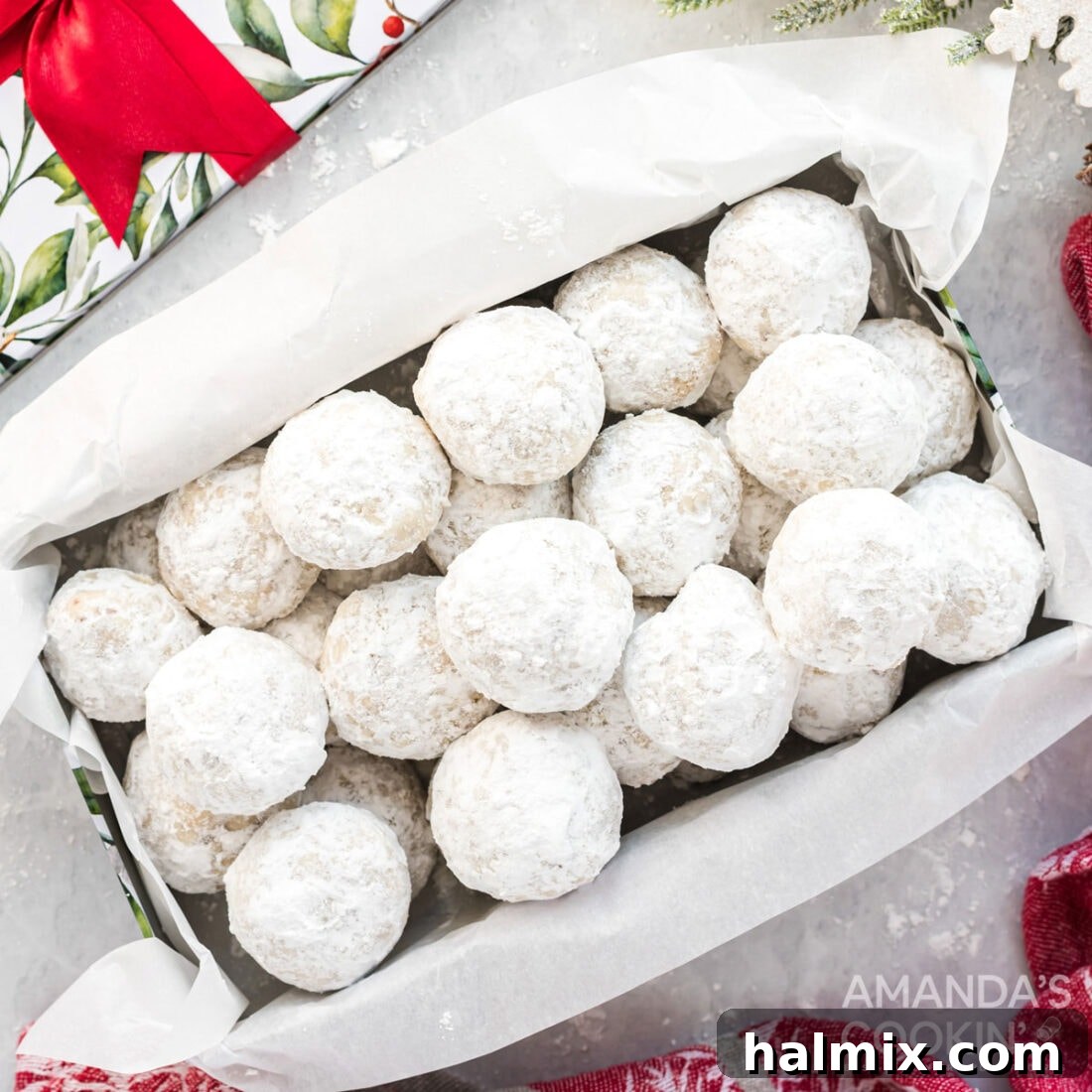 A charming box generously filled with delicate snowball cookies, each perfectly coated in a cloud of powdered sugar, making them an ideal holiday treat.