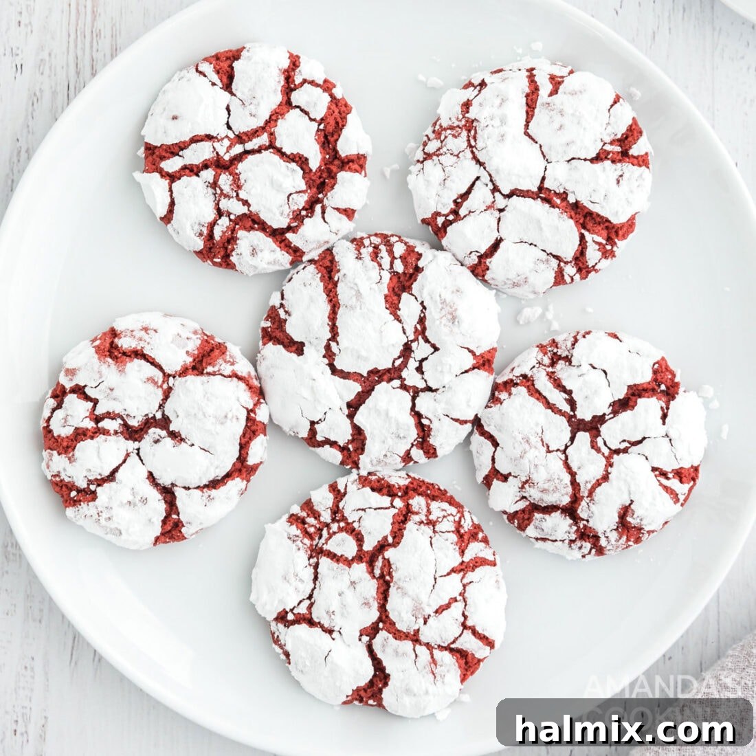 A beautifully arranged plate of vibrant red velvet crinkle cookies, generously dusted with powdered sugar, creating a festive look perfect for holiday gatherings.