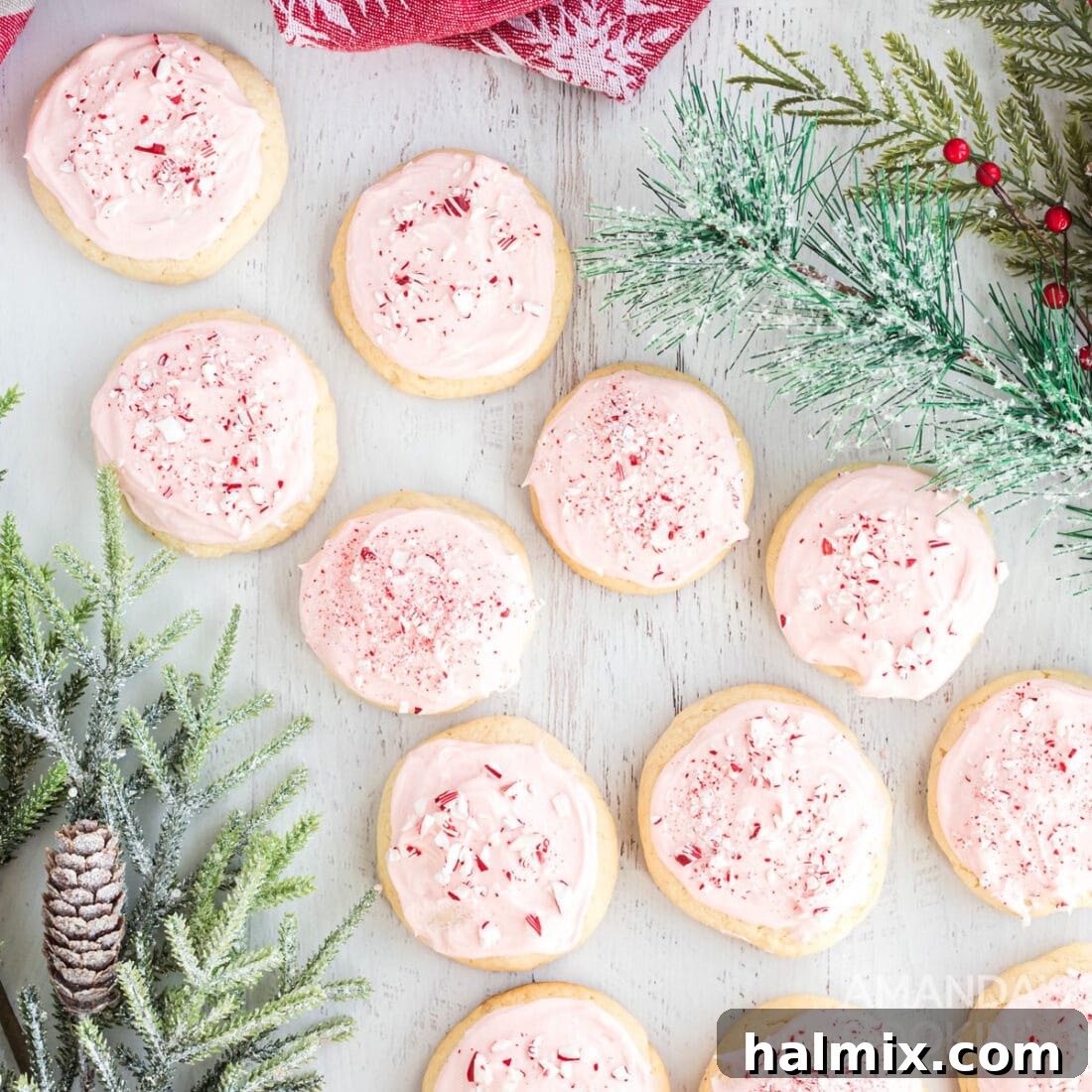 Close-up of elegantly pink frosted peppermint cookies, generously adorned with glistening crushed candy canes, showcased on a pristine white serving plate.