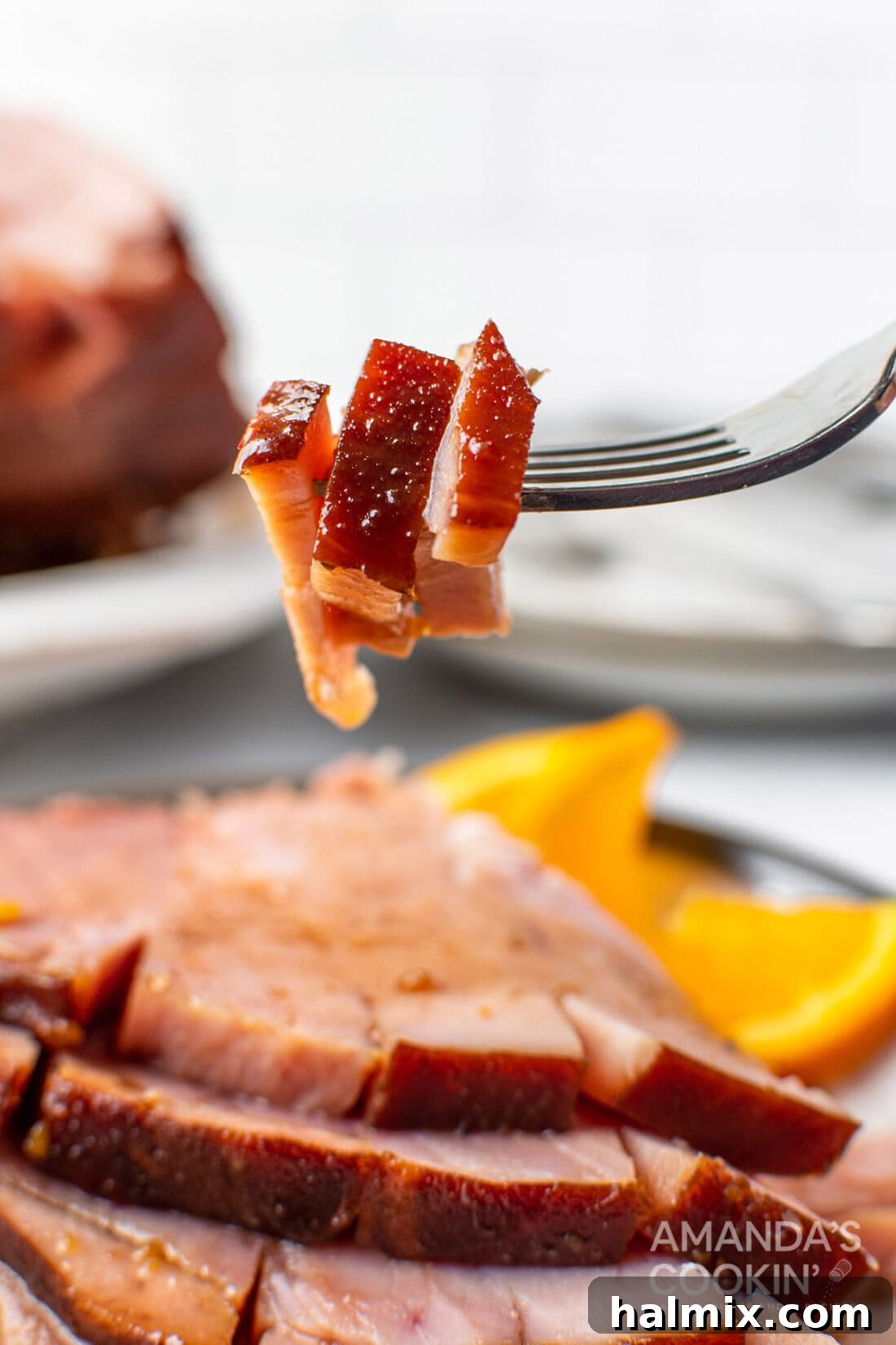 Close-up of a fork holding tender slices of orange bourbon glazed ham