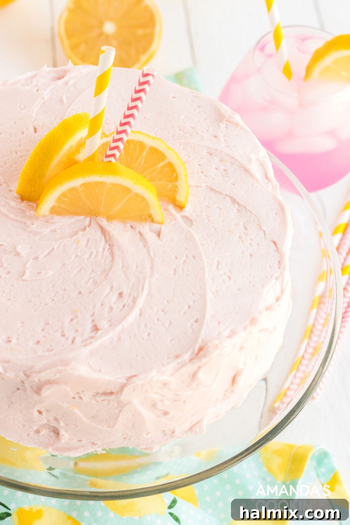 Pink lemonade cake on a platter, garnished with lemon slices and straws