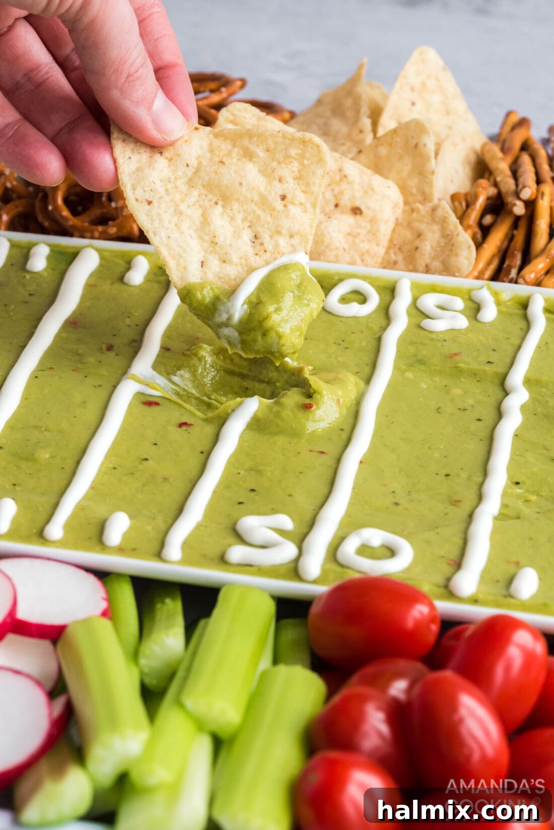 Close-up shot of a hand dipping a crispy tortilla chip into a rich, green guacamole, highlighting the deliciousness of the football party tray.