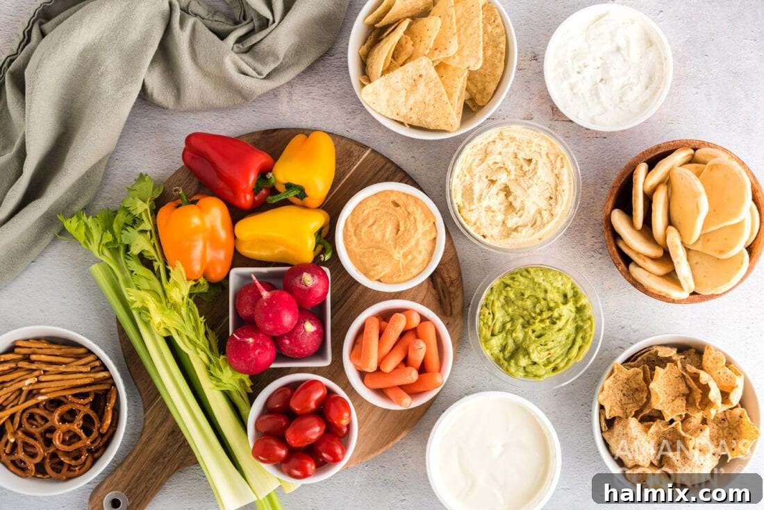 An overhead shot showcasing all the fresh ingredients laid out before assembly, including various dips, colorful vegetables, and an assortment of crackers and chips for a football party tray.