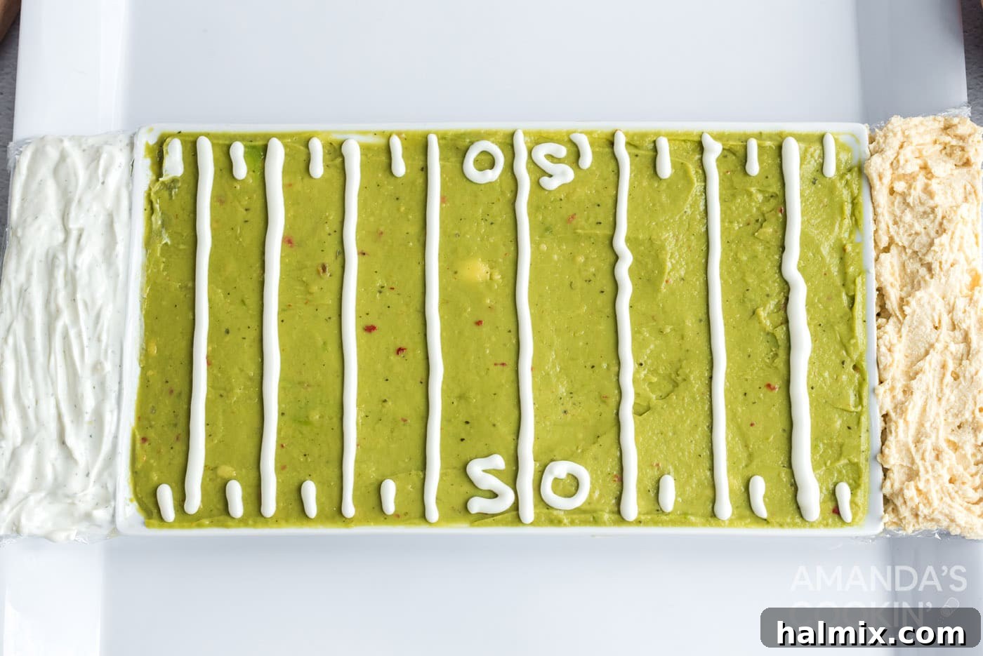 The football party tray with guacamole and sour cream lines, flanked by distinct end zones filled with hummus and French onion dip.