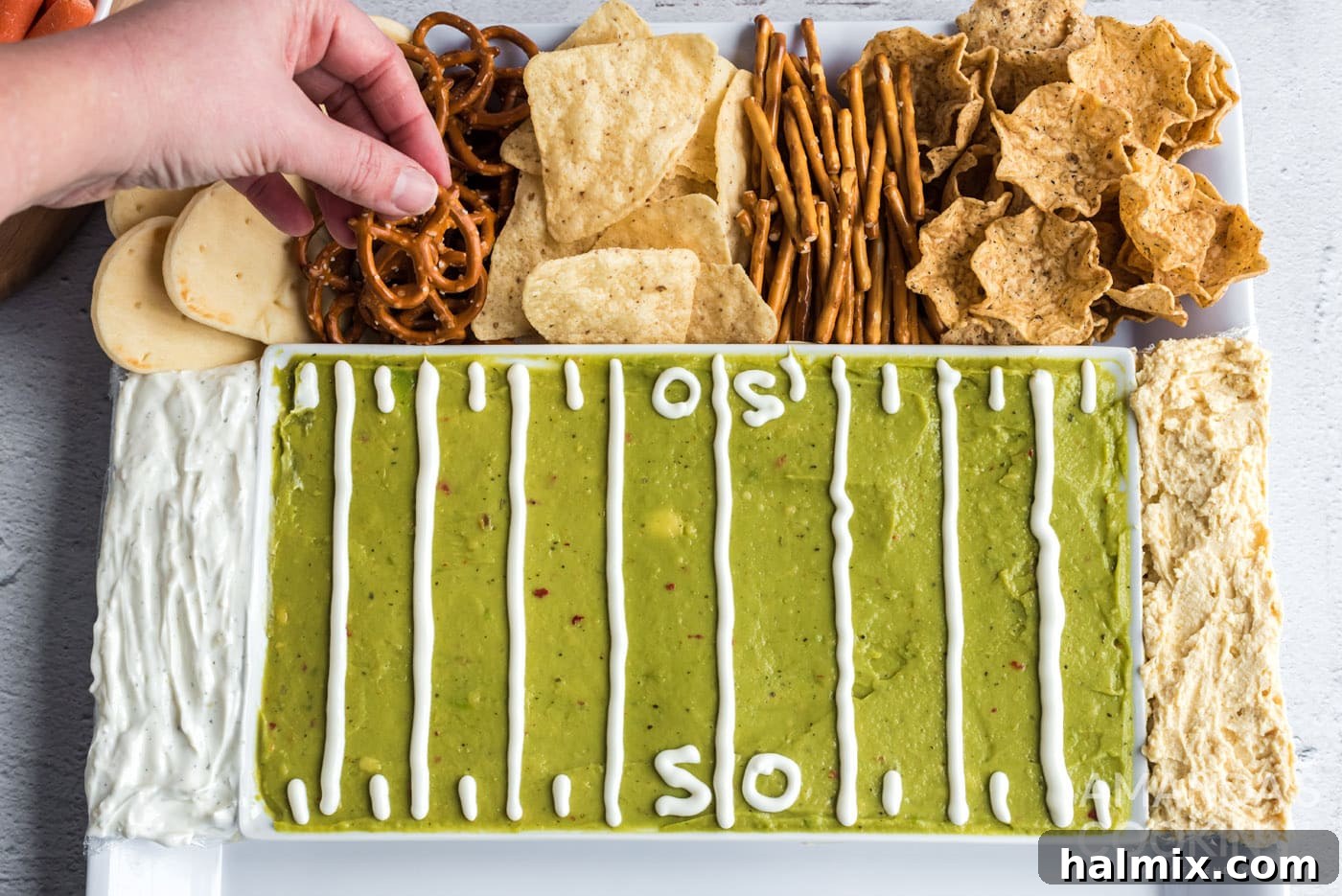 A hand reaching for a crispy pretzel from the beautifully arranged football party tray, surrounded by various dippers.