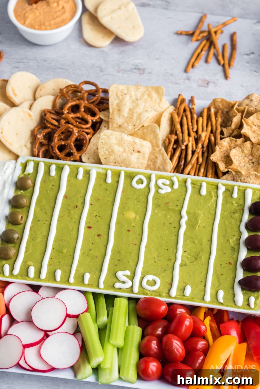 The ultimate football party tray, overflowing with an appealing mix of guacamole, creamy dips, and a wide variety of fresh vegetables and crunchy snacks, perfect for sharing.