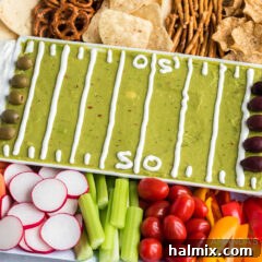 Overhead view of a football party tray with guacamole, various dips, and dippers arranged on two platters.