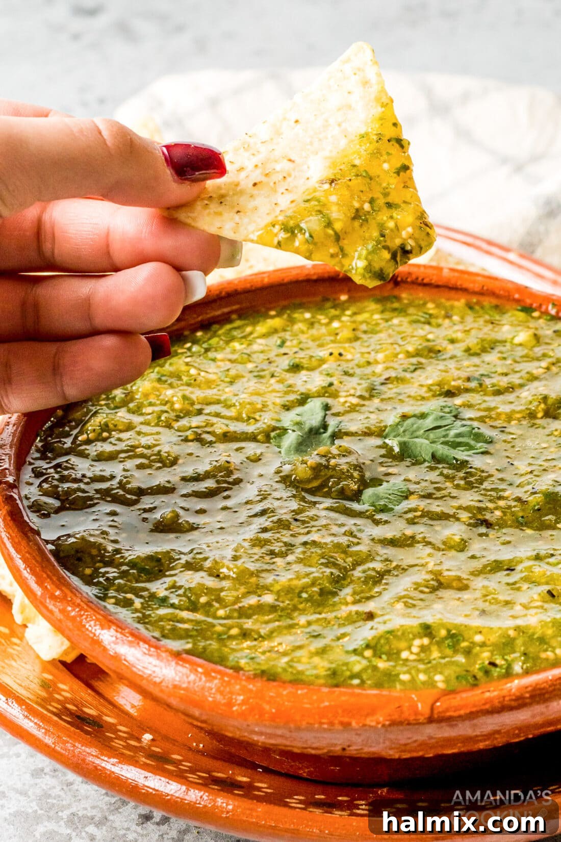 woman's hand scooping green salsa with a tortilla chip