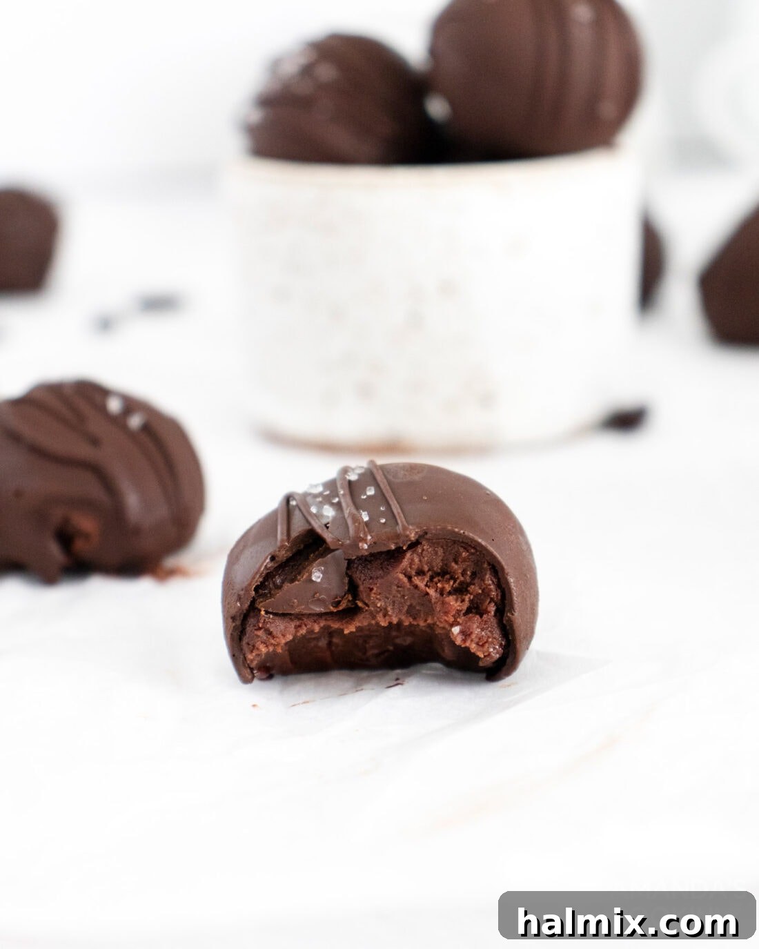 A perfectly crafted mocha truffle with a bite taken out, revealing its rich, dark interior. It's coated in a thin layer of chocolate and lightly dusted with sea salt.