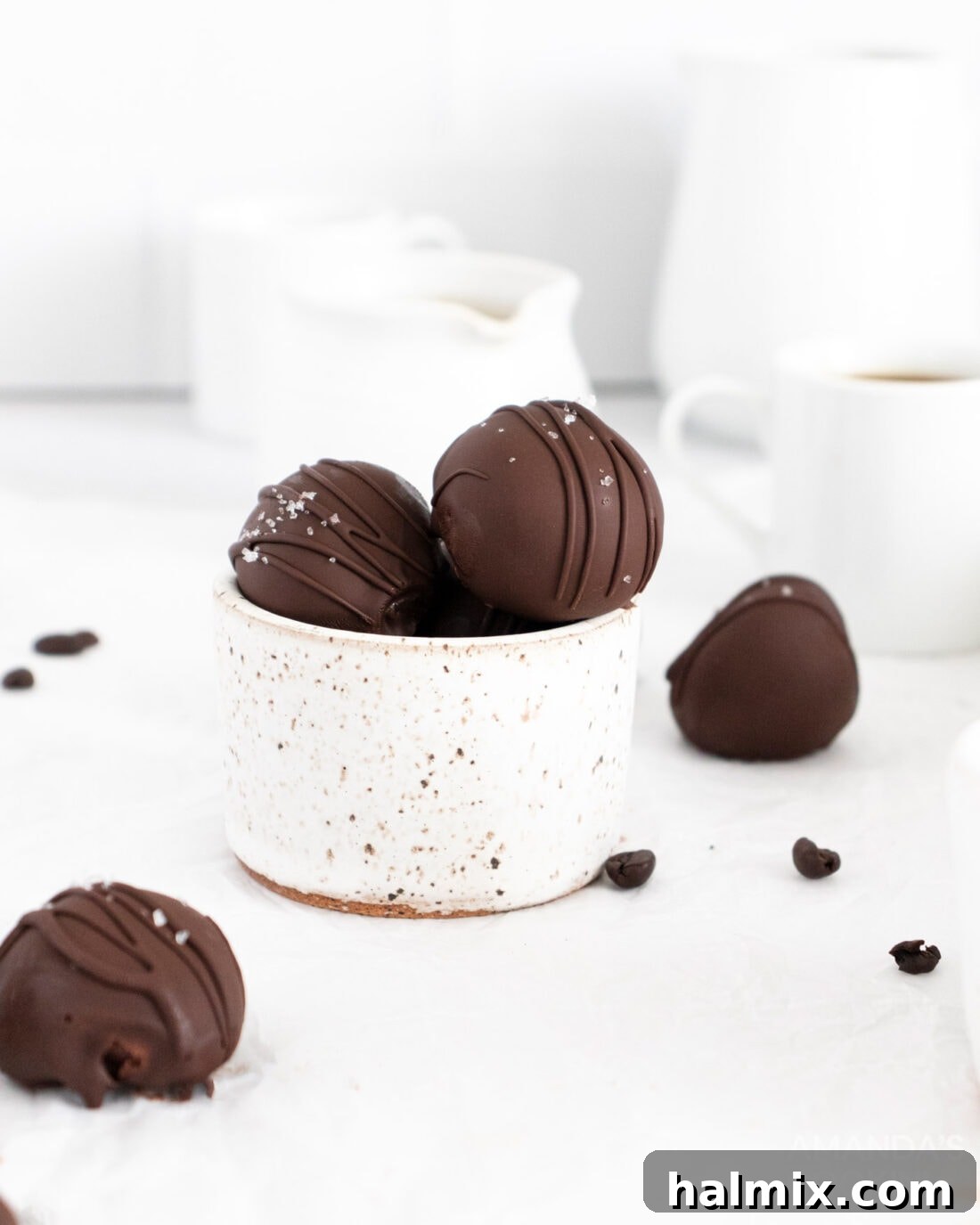 A ceramic bowl brimming with freshly made mocha truffles, each glistening with a smooth chocolate coating. Some are decorated with a light drizzle of chocolate.