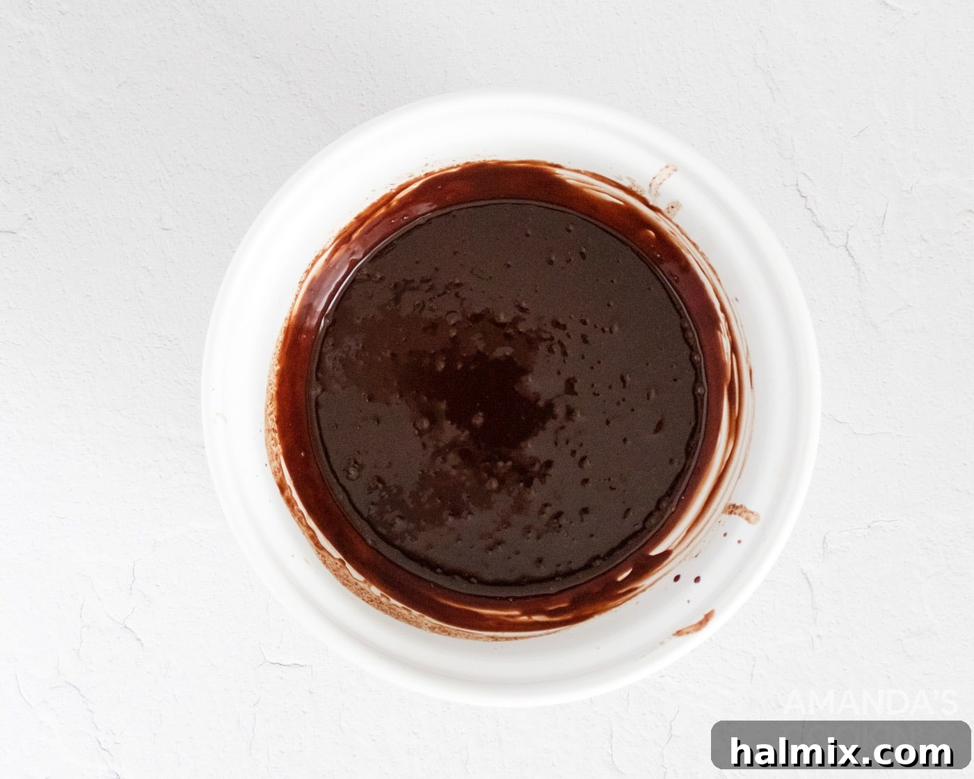 A bowl of melted chocolate and coconut oil, perfectly smooth and ready for dipping the mocha truffles, highlighted by a wooden spoon.