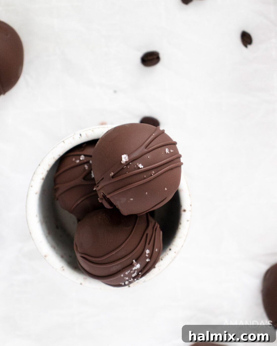 An inviting overhead shot of a white dish filled with beautifully arranged mocha truffles. Some are topped with a delicate sea salt sprinkle and chocolate drizzle.