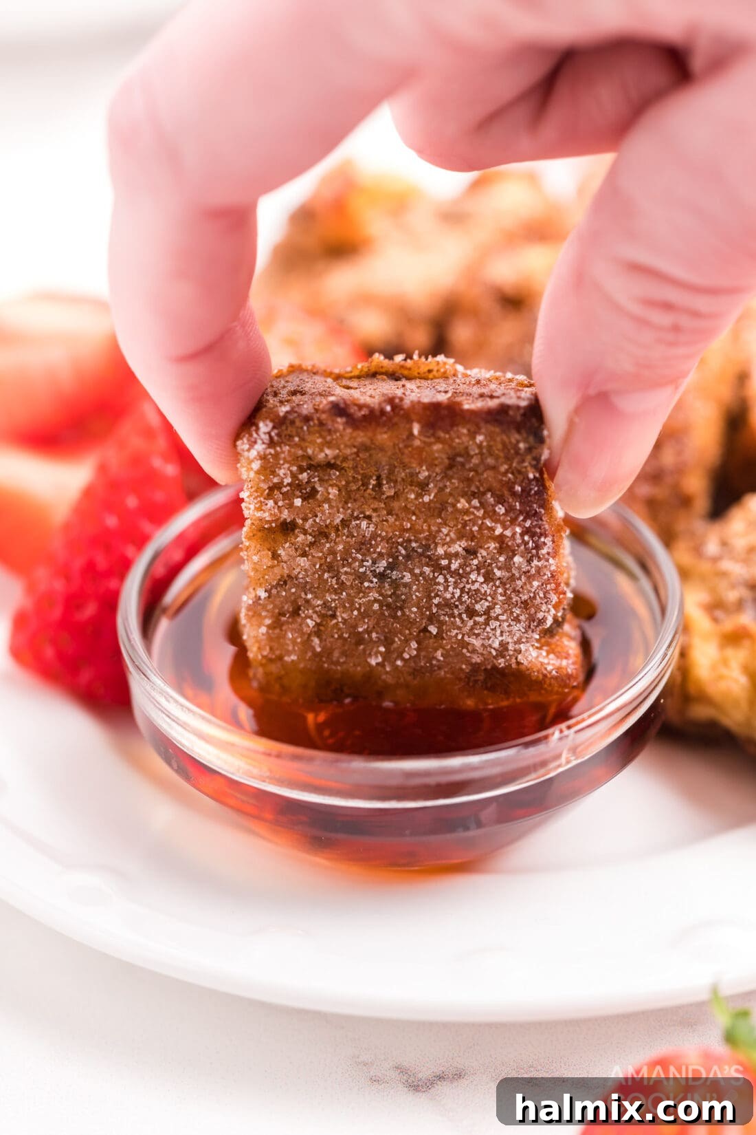 Air Fryer French Toast Poppers 2 Dipping a golden Air Fryer French Toast Bite into maple syrup, ready to enjoy a sweet breakfast.