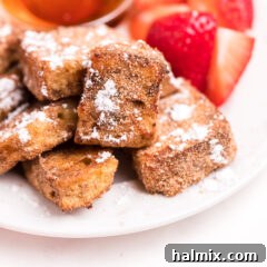 Air Fryer French toast bites on a plate, garnished with powdered sugar and berries.