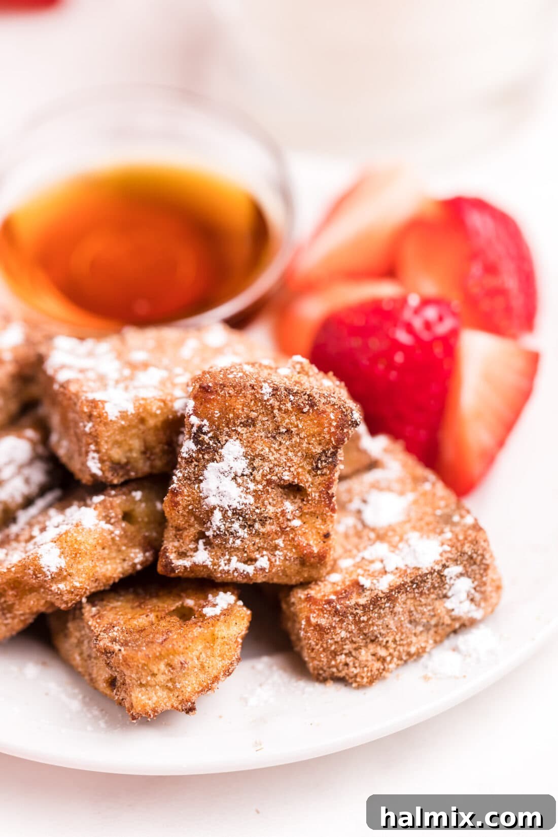 Air Fryer French Toast Poppers 3 A plate full of golden Air Fryer French Toast Bites with fresh strawberries and a drizzle of syrup, ready for a delightful breakfast.
