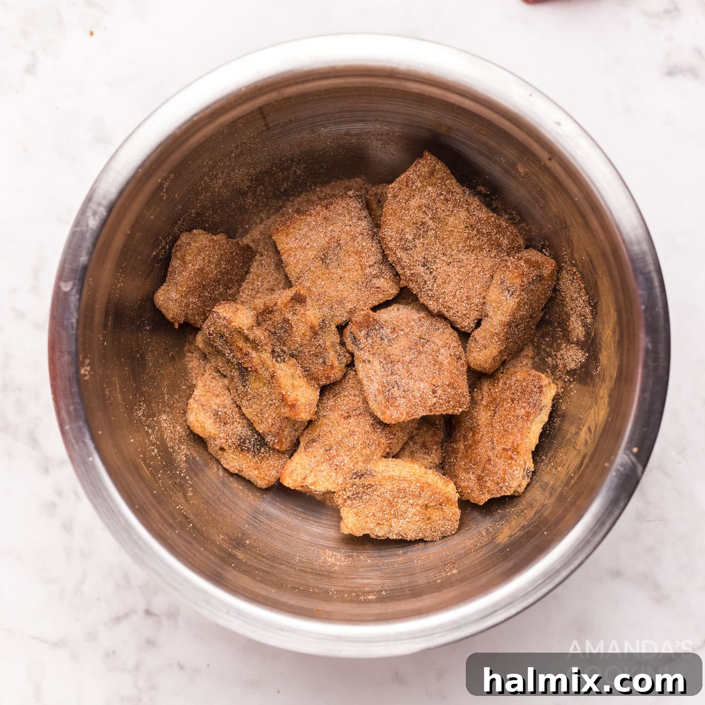 Hot French toast squares being tossed in a bowl of cinnamon sugar, ensuring a delicious and even coating.