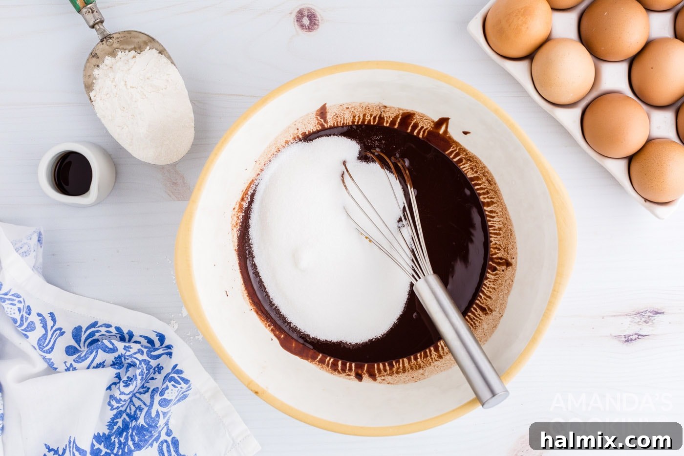 Granulated sugar being added to melted chocolate and butter mixture