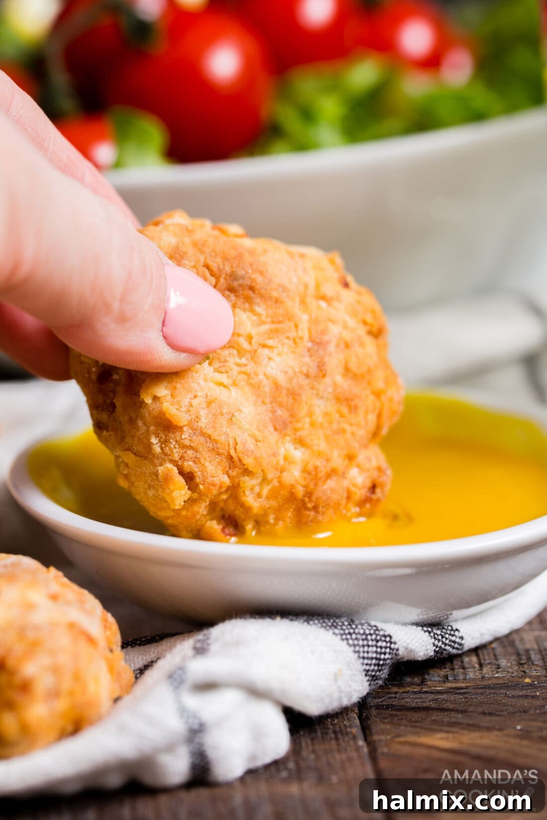 A hand dipping a freshly made air fryer chicken nugget into a vibrant yellow mustard sauce, highlighting its crispy texture.