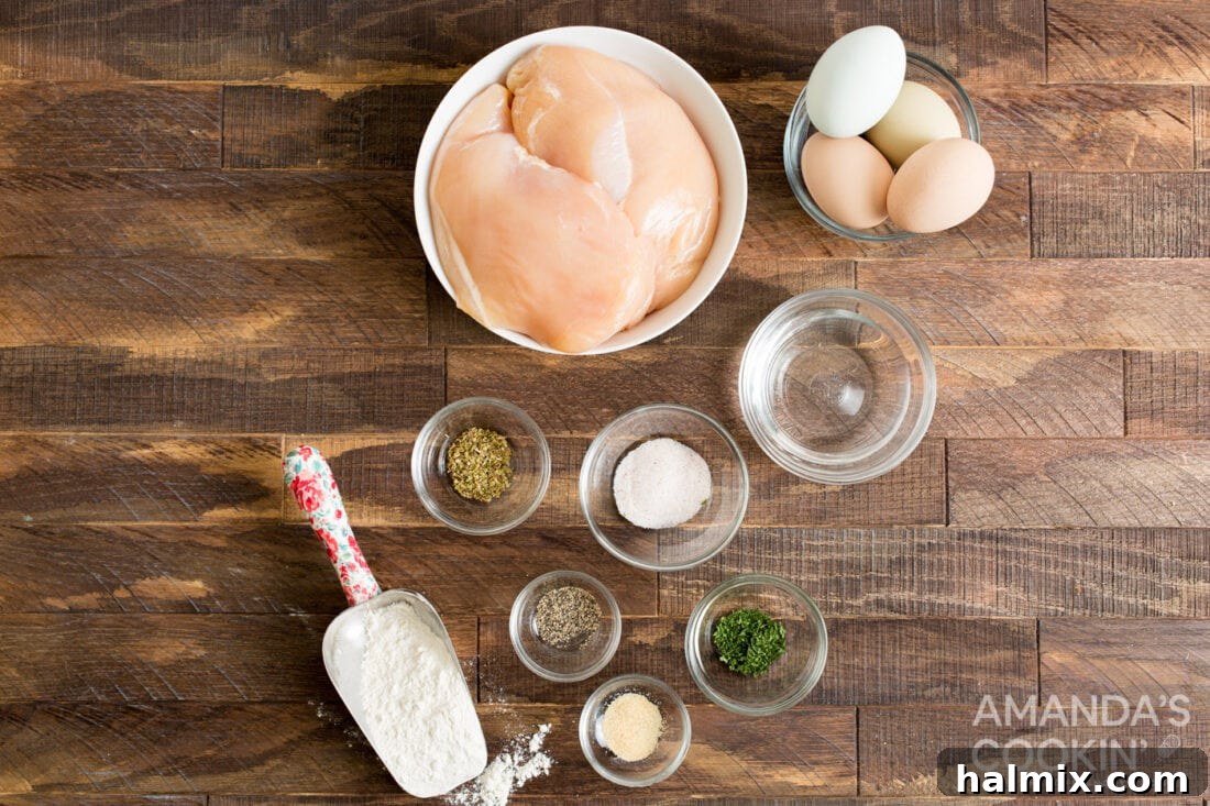 A clear glass bowl filled with boneless, skinless chicken breasts sits alongside smaller bowls of flour, eggs, and various spices.