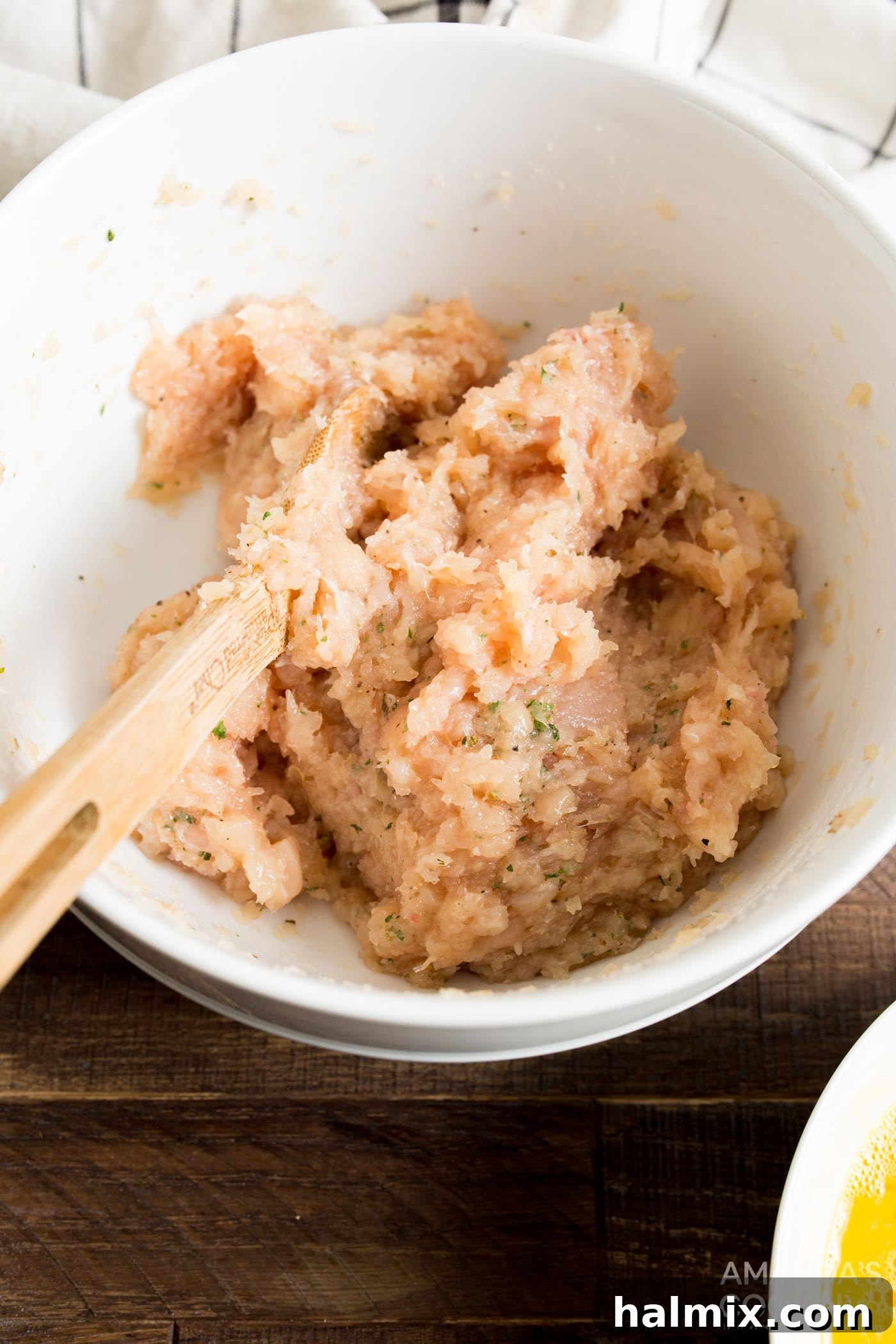 A bowl containing finely processed chicken paste mixed with a blend of herbs and spices, ready for shaping.