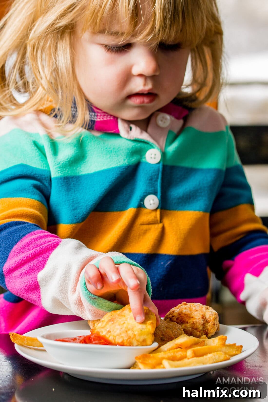 A young girl smiling and happily dipping a fresh air fryer chicken nugget into a bowl of sauce, ready to eat.