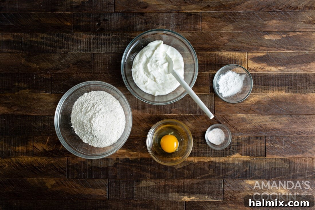 A flat lay of the 5 simple ingredients for air fryer bagels: self-rising flour, baking powder, salt, non-fat Greek yogurt, and an egg for egg wash.