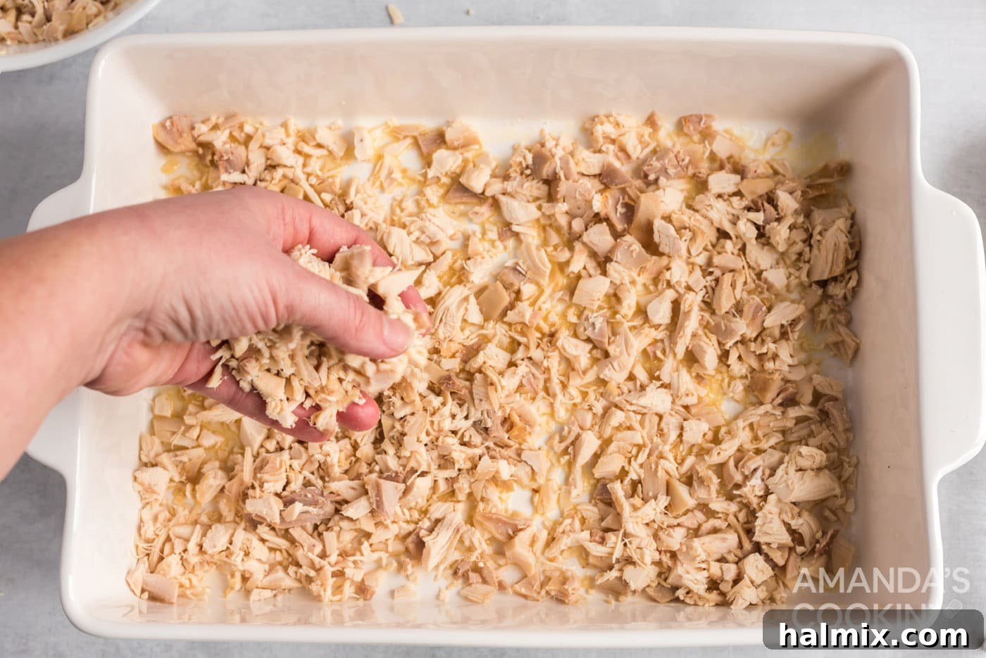 Cooked chicken pieces being spread over melted butter in a baking dish.