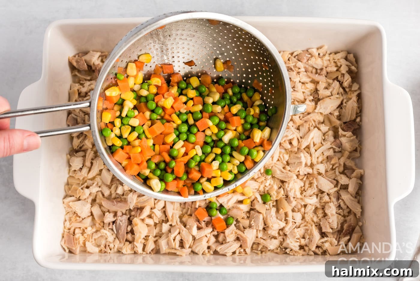 Drained frozen mixed vegetables being carefully spread over the chicken layer in the casserole dish.