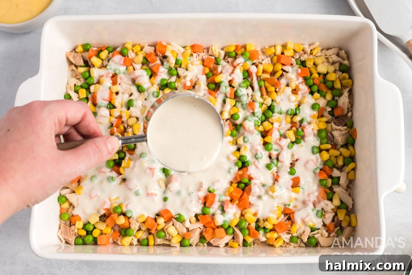 The milky flour mixture being slowly and gently poured over the vegetable and chicken layers in the casserole dish.