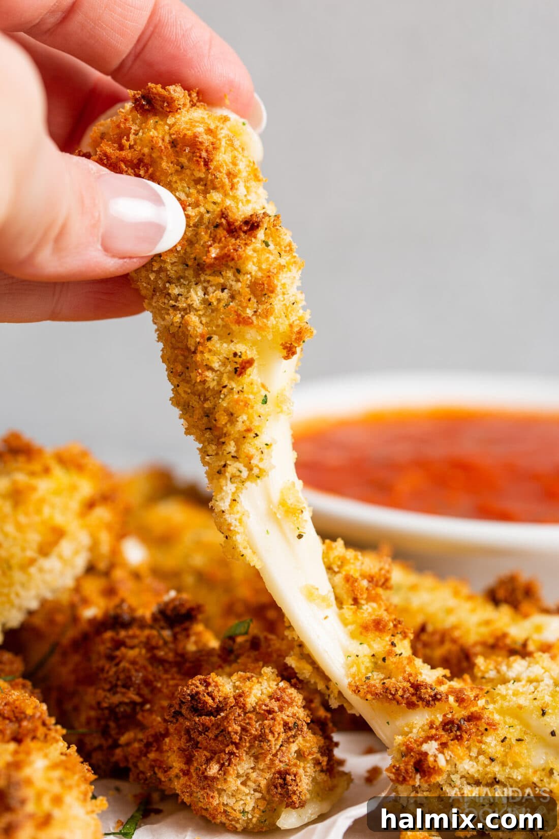 Lifting a melty, golden-brown air fryer mozzarella stick, showing off its irresistible cheese pull, ready to be dipped.