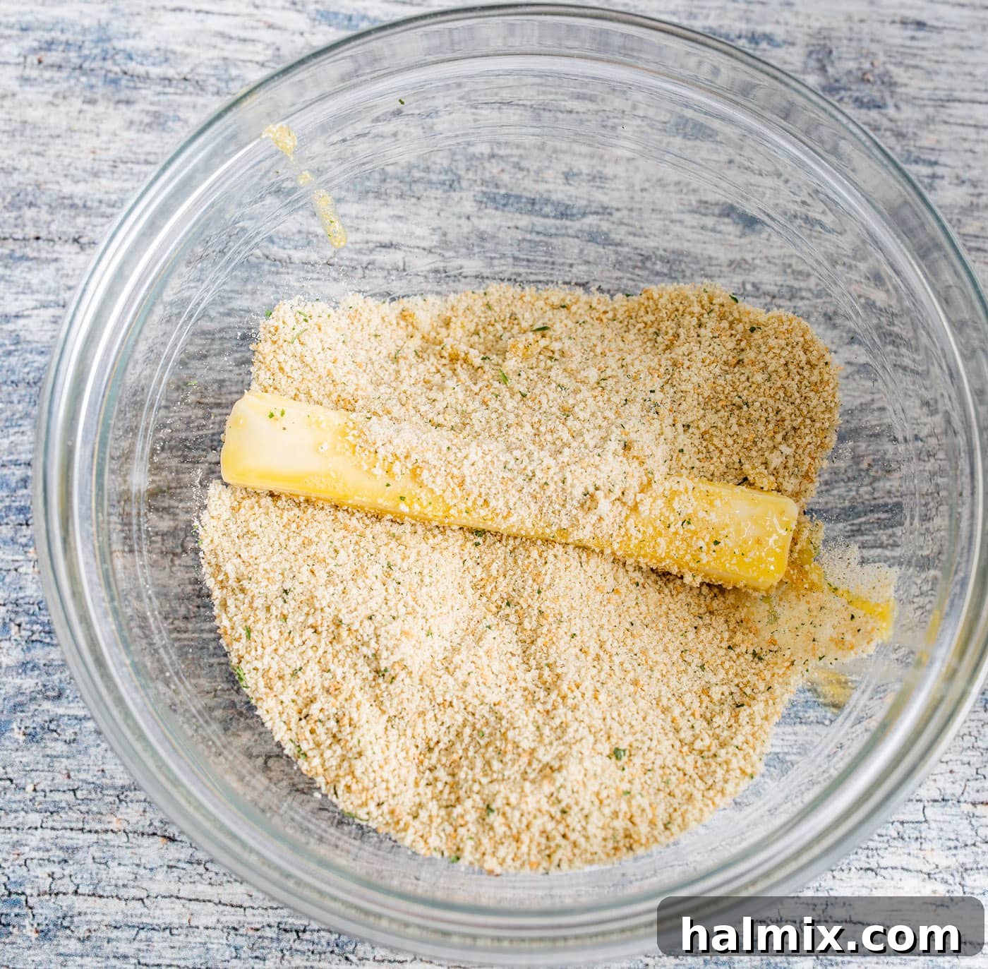A cheese stick being coated in a bowl of Italian bread crumbs for the first breading layer.