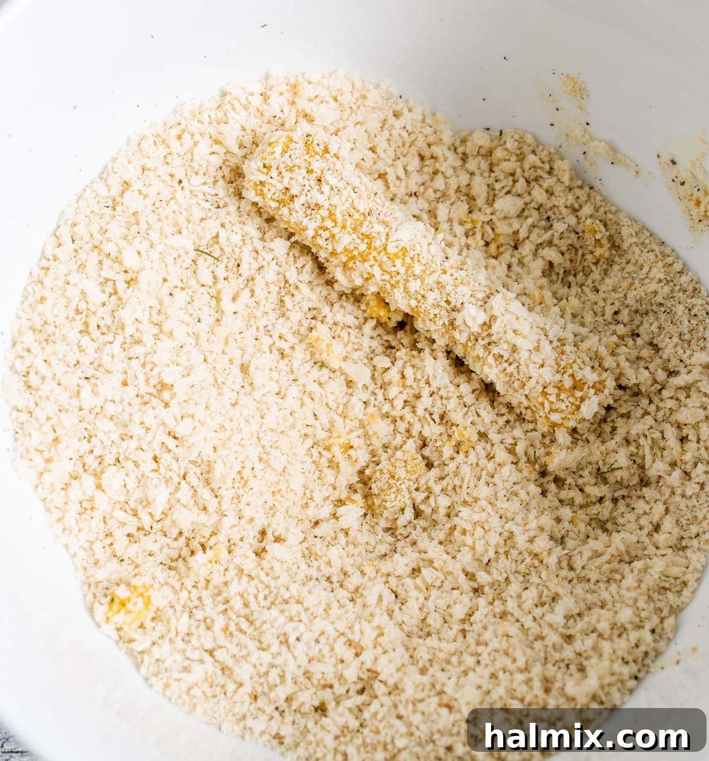 A cheese stick fully coated in a mixture of Panko and Italian breadcrumbs, ready for air frying.