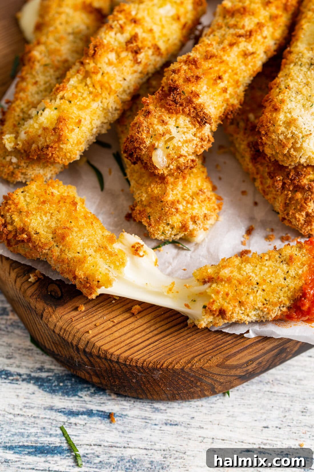 A close-up shot of a melty, golden-brown air fryer mozzarella stick on a rustic wooden cutting board, showcasing its enticing stretchiness.