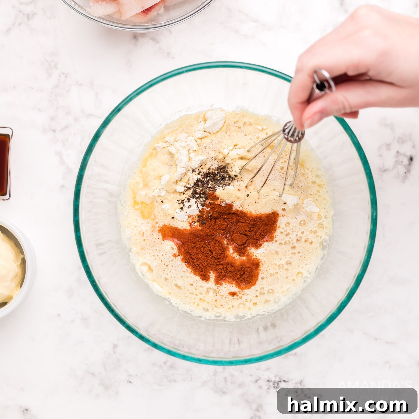 Seasonings being added to the beer batter mixture in a bowl.