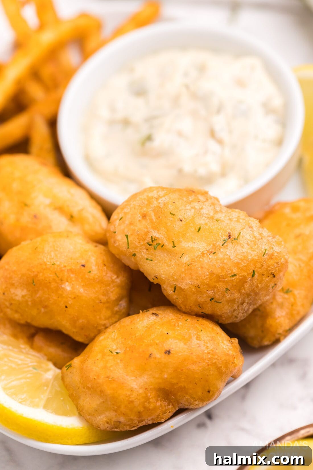 A serving of golden beer battered fish nuggets presented on a plate with a side of creamy tartar sauce.