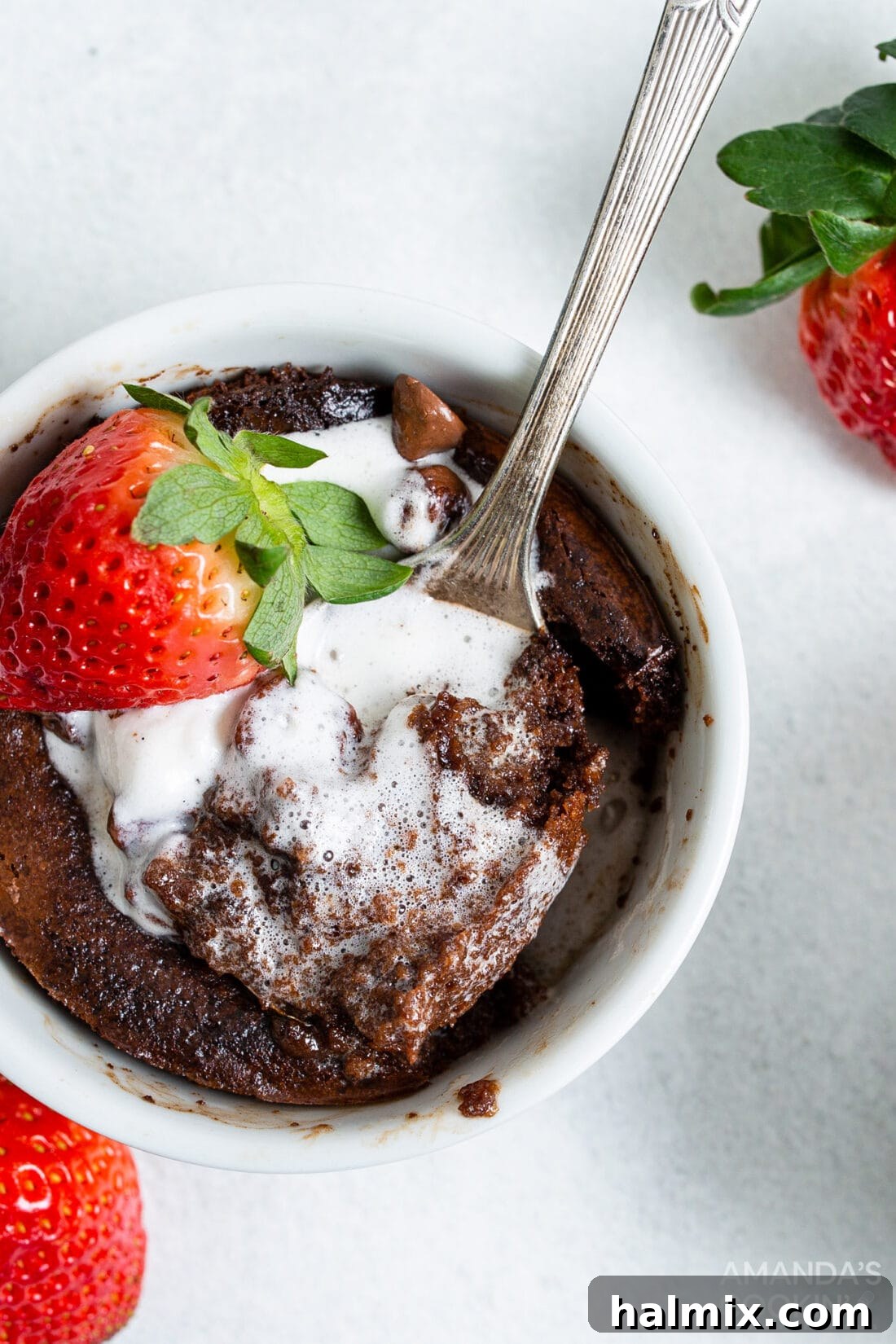 A delectable air fryer brownie in a ramekin, adorned with a scoop of vanilla ice cream and fresh strawberries, ready to be enjoyed.