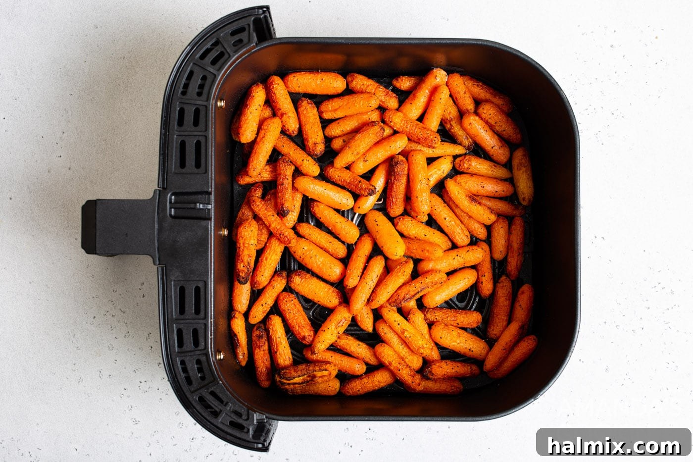 Deliciously cooked air fryer carrots, topped with shredded parmesan and fresh parsley, in the air fryer basket.