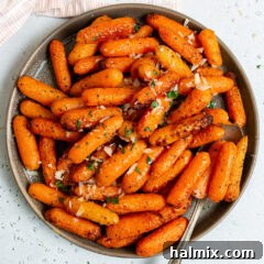 Close-up of golden air fryer carrots on a white plate, garnished with fresh herbs.